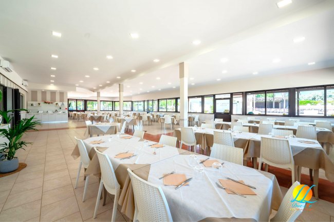 Ampia sala ristorante con tavoli apparecchiati e sedie bianche.