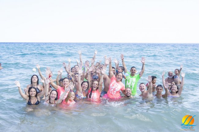 Un gruppo di persone che sorridono e alzano le mani nell'acqua di mare.