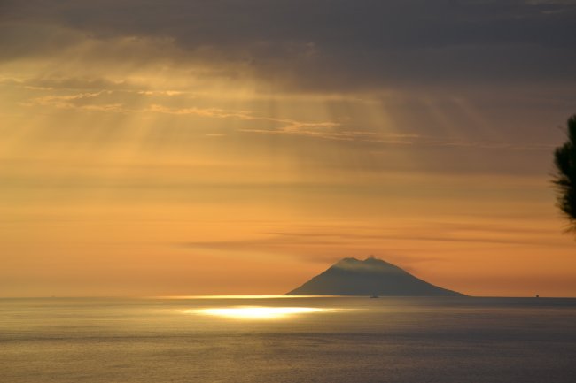 Tramonto sul mare con un'isola all'orizzonte.