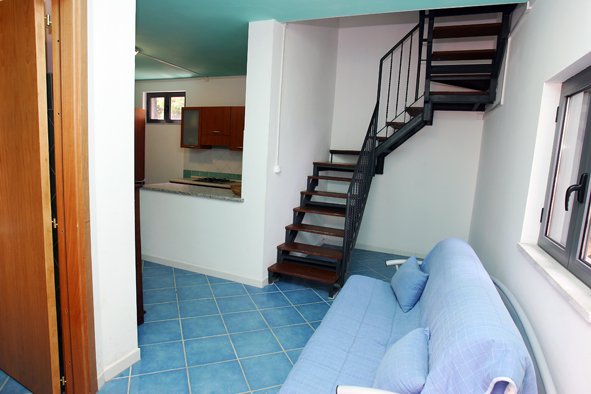 Interno con divano blu, scala a chiocciola e cucina.
