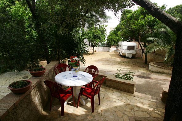 Tavolo rotondo con sedie rosse in un giardino con alberi e roulotte.
