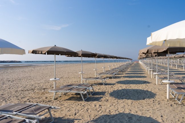 Spiaggia con file di lettini e ombrelloni chiusi che si estendono verso il mare.