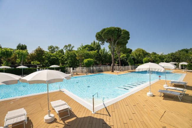 Piscina all'aperto con ombrelloni bianchi e lettini su una terrazza in legno.