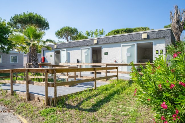 Edificio con piccole unità abitative, rampe di legno, palmizi e fiori.