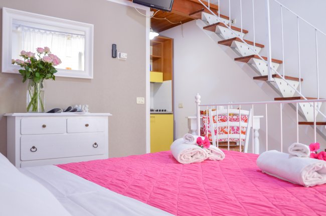 Letto con copriletto rosa, scale in legno, vaso di fiori.