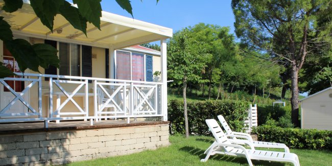Veranda di una casa mobile con sedie a sdraio su un prato verde.