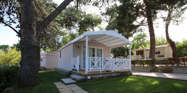 Bungalow con veranda bianca, circondato da alberi.
