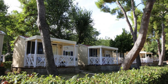Bungalow con verande bianche circondati da alberi alti.