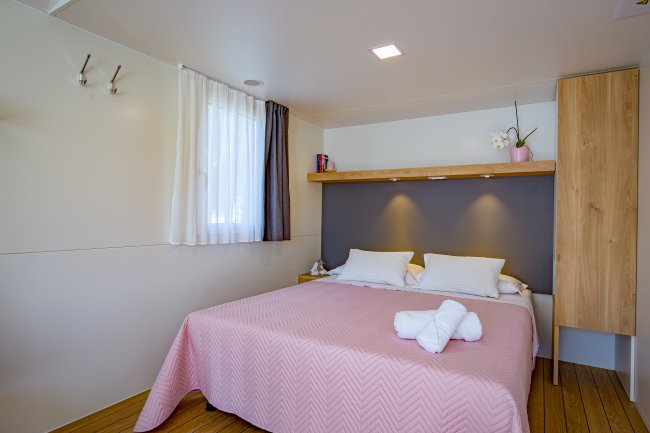 Letto con copriletto rosa, finestra con tende bianche e nere.