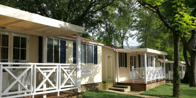 Case mobili beige con terrazze e alberi ombreggianti.