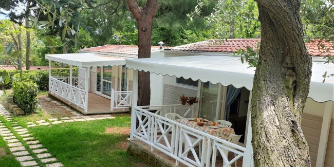 Verande bianche di bungalow in giardino verde con alberi.