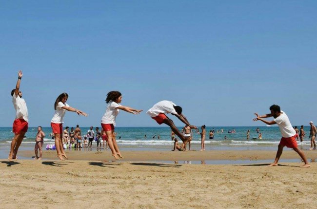 Persone che fanno acrobazie sulla spiaggia davanti al mare.