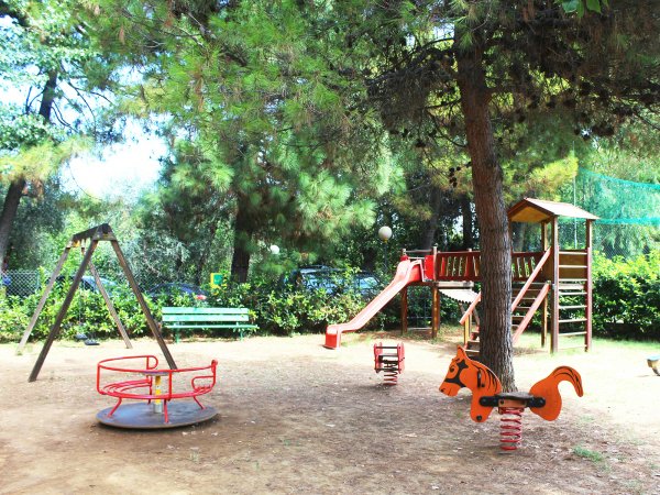 Un parco giochi con altalena, giostra rossa e scivolo tra alberi.