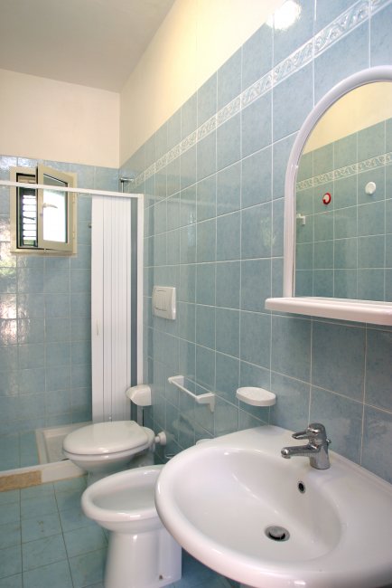 Bagno con lavabo, specchio, WC e doccia, piastrelle azzurre.