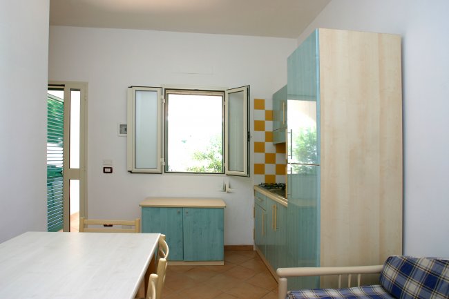 Una cucina con mobili azzurri, tavolo bianco e finestra aperta.