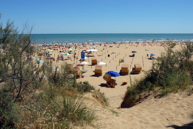 Spiaggia affollata con ombrelloni e mare calmo.