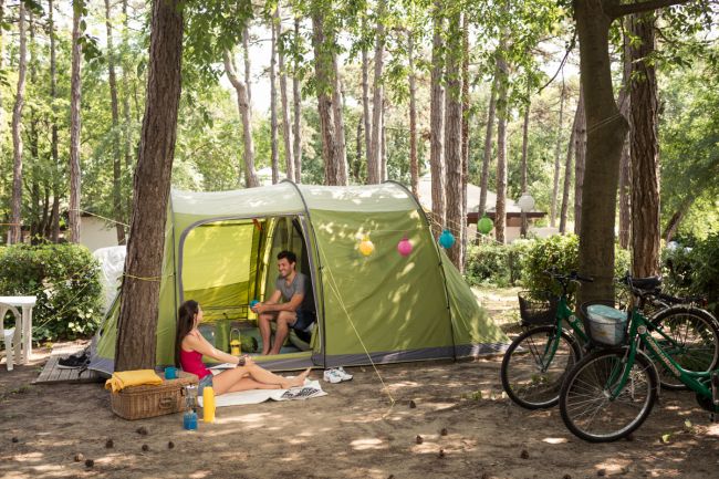 Due persone sedute accanto a una tenda in un campeggio, con biciclette e decorazioni colorate.