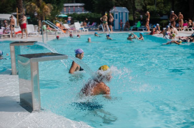 Piscina estiva affollata con persone che si rinfrescano.
