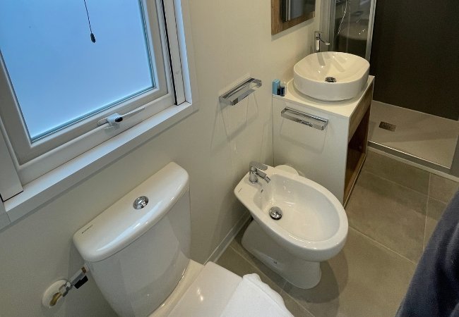 Un bagno con wc, bidet, lavandino rotondo, doccia e finestra.