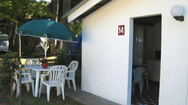 Bungalow bianco con sedie e tavolo fuori.
