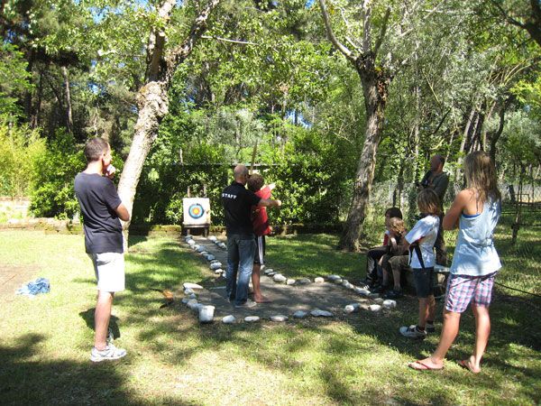 Persone fanno tiro con l'arco in un bosco, seguiti da un istruttore.