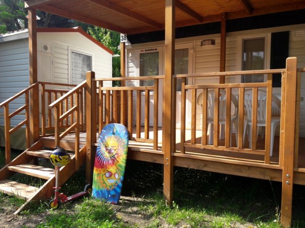 Bungalow con veranda in legno, monopattino e tavola da bodyboard colorata.