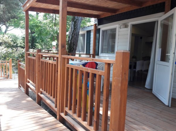 Veranda in legno con ringhiera e accesso a una casa mobile.