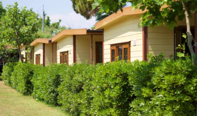 Bungalow gialli con tetti marroni dietro una siepe verde.