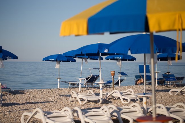 Spiaggia con lettini, ombrelloni blu e mare calmo sullo sfondo.