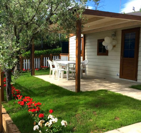 Casetta con veranda, sedie da giardino bianche e prato con fiori rossi.