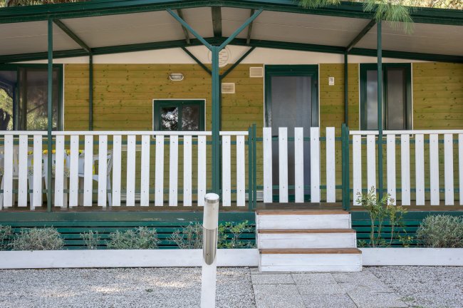 Casa mobile con veranda, recinzione bianca e gradini.