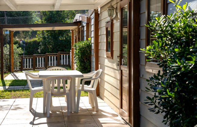Tavolo e sedie bianche su una veranda con giardino.