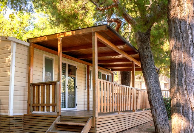 Casa mobile con veranda di legno, situata sotto grandi alberi.