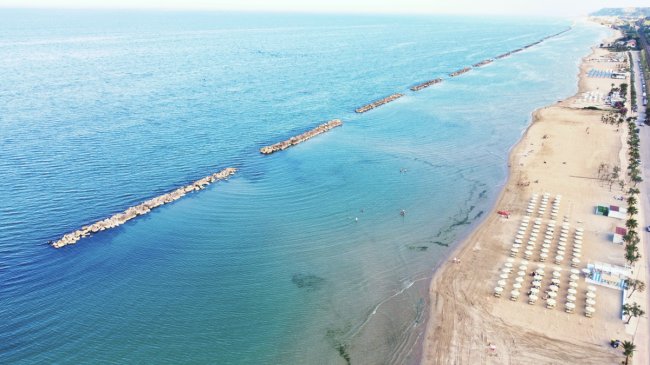 Spiaggia con ombrelloni e mare, frangiflutti visibili.