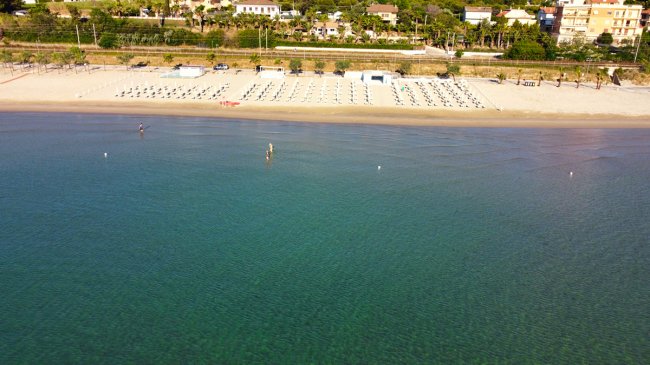 Spiaggia sabbiosa con ombrelloni allineati e mare calmo.