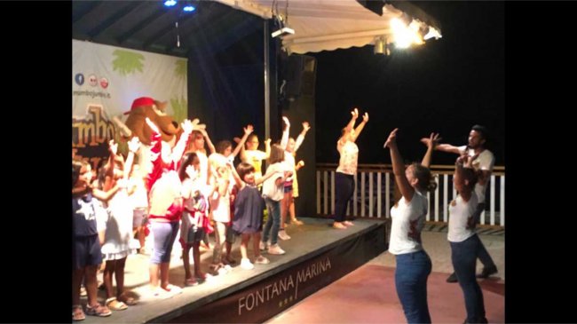 Bambini e animatori danzano su un palco al chiuso.