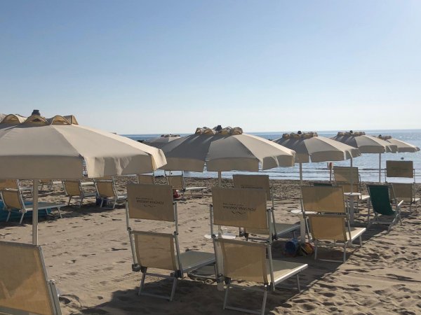Ombrelloni e lettini sulla spiaggia, con mare calmo sullo sfondo.