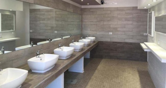 Un bagno moderno con sei lavandini bianchi su un lungo bancone.