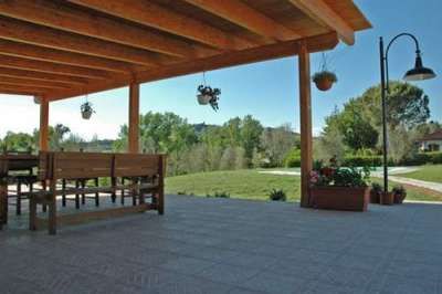 Portico con tavolo e panche, vasi appesi, giardino sullo sfondo.