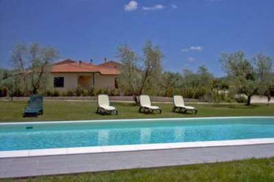 Una piscina azzurra con sedie a sdraio, casa sullo sfondo e cielo blu.