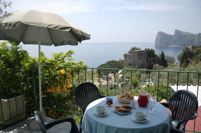 Tavolo all'aperto con colazione vista mare e torre in lontananza.