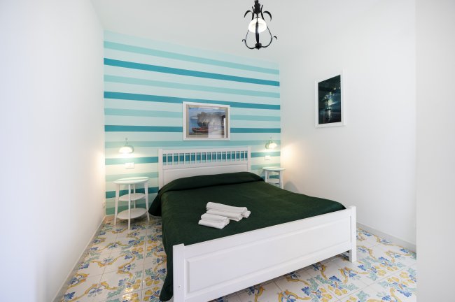 Camera con letto matrimoniale bianco, parete a righe blu e lampadari pendenti.
