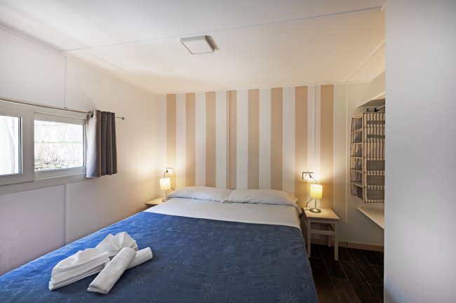Camera con letto matrimoniale, pareti a strisce beige, due lampade e finestra laterale.