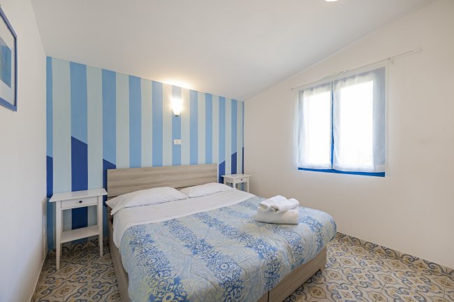 Una camera da letto con pareti a strisce blu e bianche, letto matrimoniale e finestra.