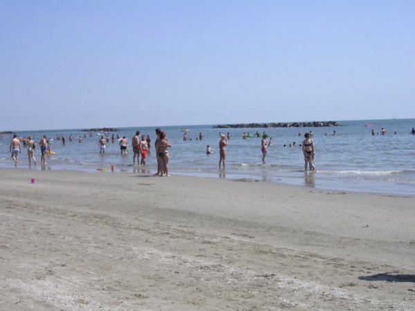 Persone in spiaggia con acqua bassa e cielo azzurro.