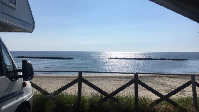 Vista sul mare con un camper e una spiaggia sabbiosa.