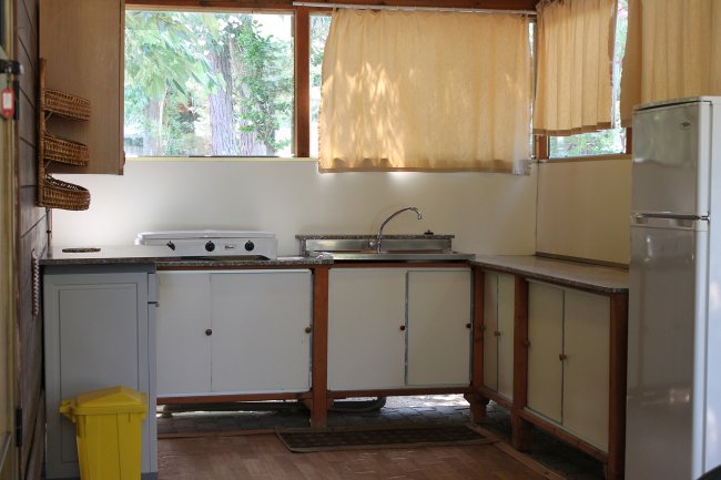 Cucina semplice con lavandino, fornelli e finestre coperte da tende gialle.