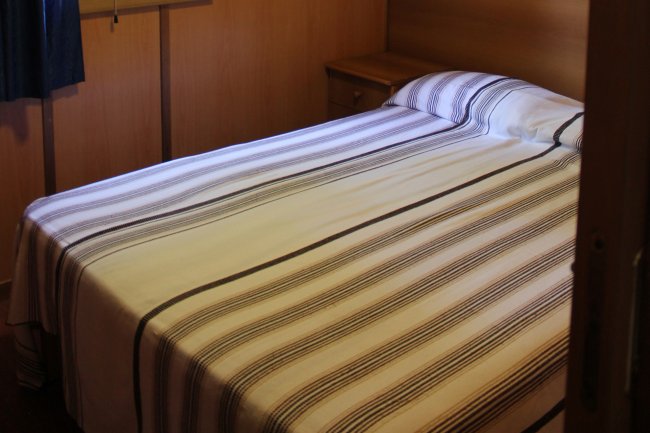 Una camera da letto con letto matrimoniale e copriletto a righe. Pareti in legno chiaro.