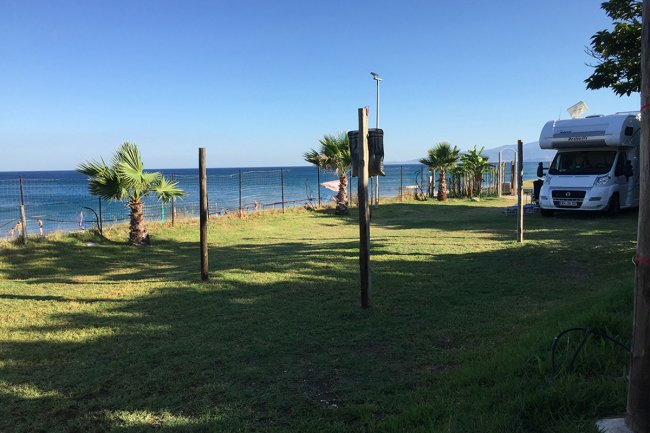 Un camper vicino a un prato verde con vista sul mare e palme.
