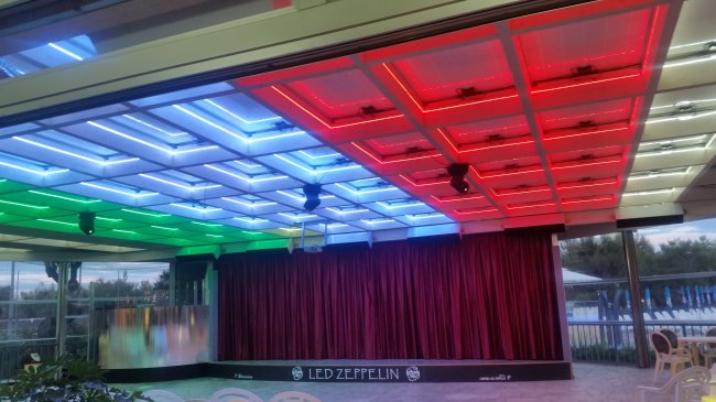 Soffitto colorato con luci a LED sopra un palco con tenda rossa.